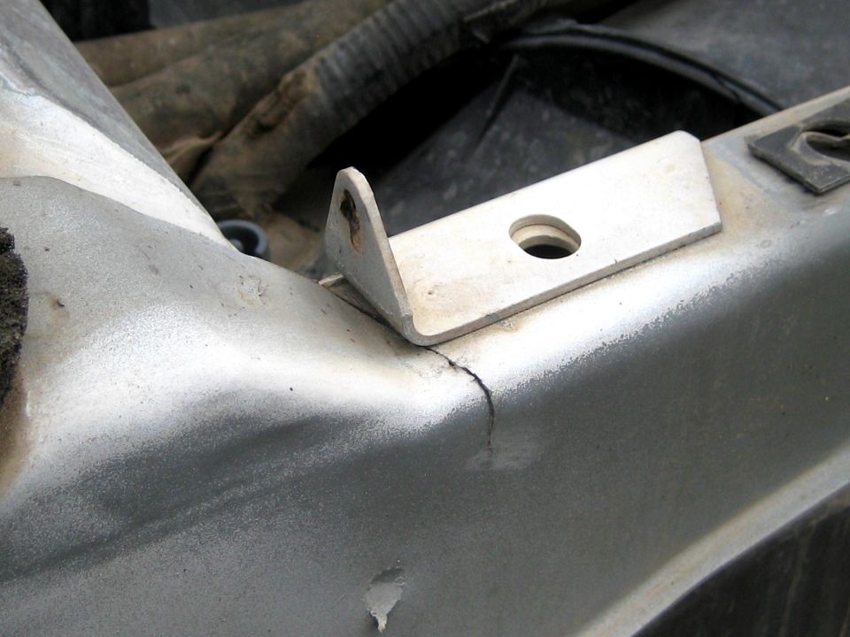 L-shaped mounting tab on inner fender rail with a crack in the sheet metal below it