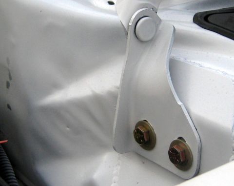 1996 Ford Bronco - A close-up view of a white painted metal hood hinge bracket is attached to a dented white metal panel.