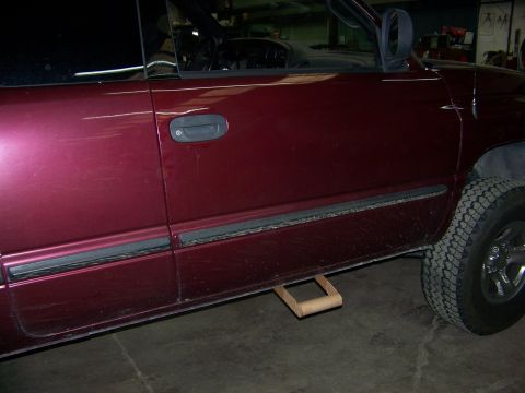 2001 Dodge 1500 - Close-up view of a maroon truck's side step, with a wooden block placed beneath it for support.