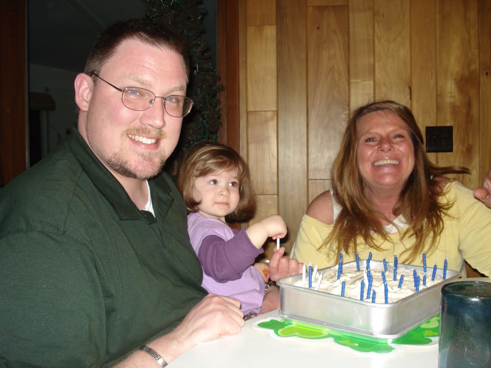 Man, woman, and child at a table with a cake covered in candles