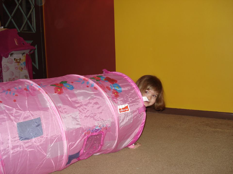 Child peeking out of a pink play tunnel with floral patterns
