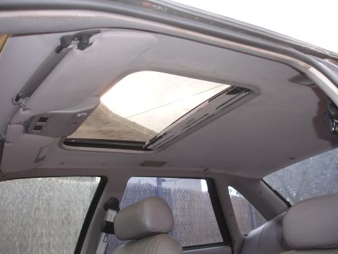 1989 Ford Taurus - The interior of a car shows a sunroof and beige seats, with a view of the exterior through the windows.
