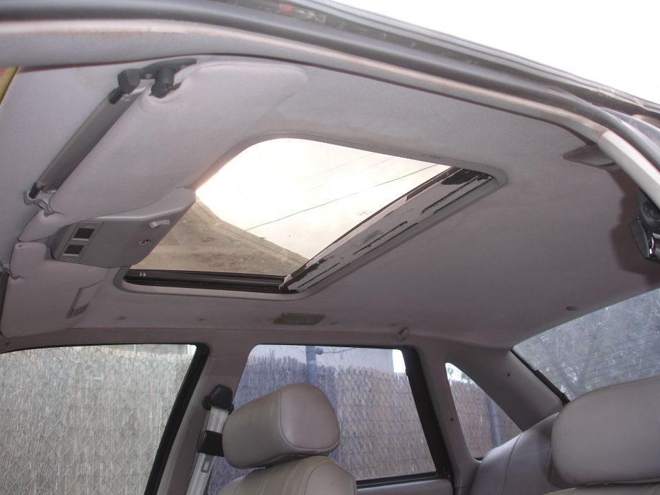 Car interior showing a grey headliner with an open sunroof, beige seats, and a rear window