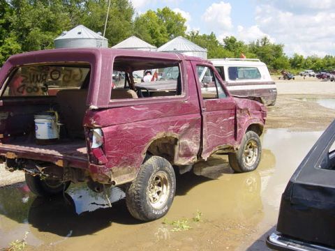 1992 Ford Bronco - A damaged maroon SUV sits in a muddy outdoor area, with other vehicles and agricultural structures visible.