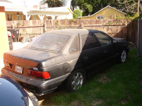 1989 Ford Taurus - A dusty 1989 Ford Taurus sits in a residential backyard next to a fence.