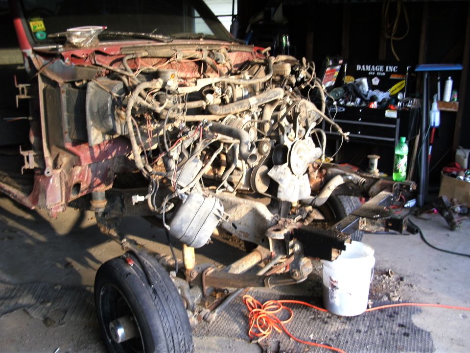 Truck chassis with engine removed, sitting in a garage with tools and a bucket nearby