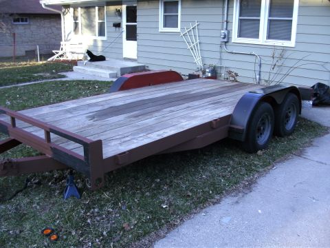 2005 Ford F-250 - A utility trailer with a wooden deck is parked on grass in front of a residential building.