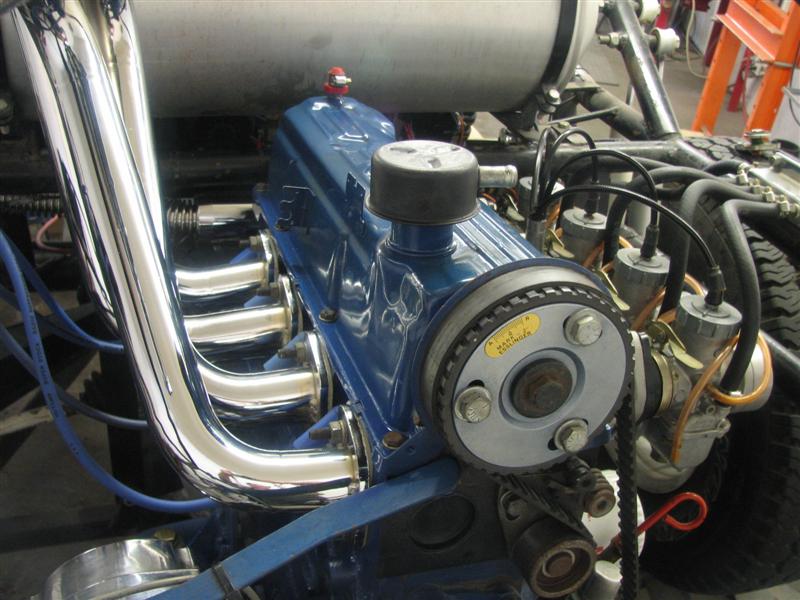 Blue engine with chrome headers, belt-drive pulley and carbs in a shop