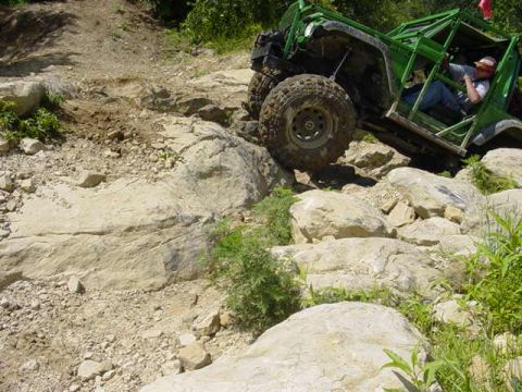 1992 Ford Bronco - A modified green off-road vehicle tackles a challenging rocky obstacle on a trail.