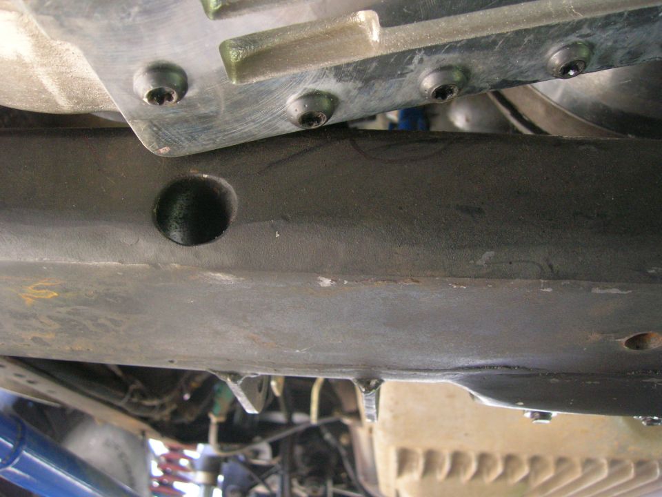 Vehicle undercarriage with black painted frame, metal plate, and suspension components