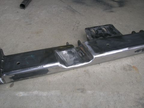 1996 Ford Bronco - A shiny chrome bumper with mounting brackets sits on a concrete floor.