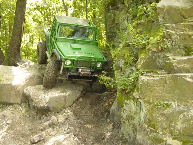 Green off-road vehicle on a rocky trail, climbing over large boulders