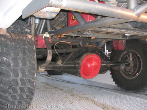 1990 Ford Bronco - Close underbody shot of an off-road truck showing leaf springs, a red-painted differential cover and large knobby tires on a trailer.