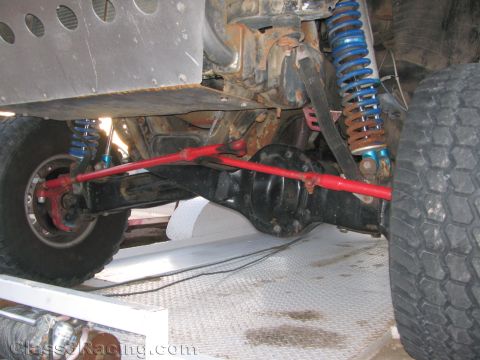 1990 Ford Bronco - Underbody view of an off-road truck front suspension with blue coilover shocks, a red drag link and the front differential.