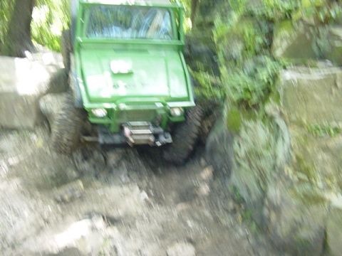 1992 Ford Bronco - A green off-road vehicle is shown from the front, tackling a challenging rocky and muddy path.