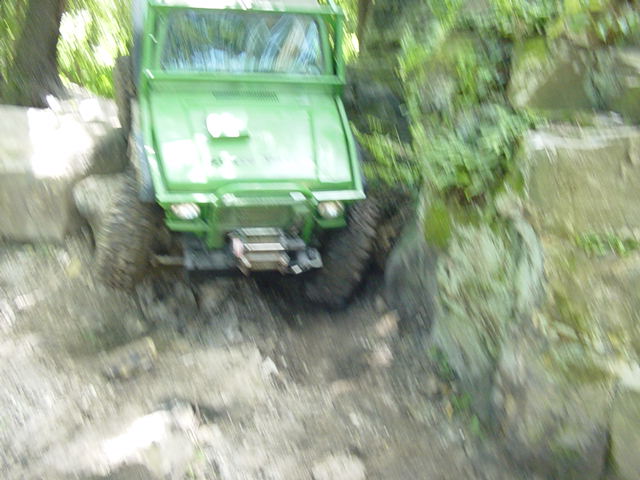 Green off-road vehicle with a winch on the front, navigating a rocky, muddy terrain