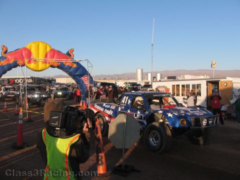 1990 Ford Bronco - blue star-themed off-road truck numbered 41 idles at a start line under a Red Bull inflatable arch as a cameraman films.