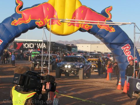 1990 Ford Bronco - Several off-road race trucks line up under a large Red Bull inflatable arch with a Yokohama banner as a cameraman films the start.