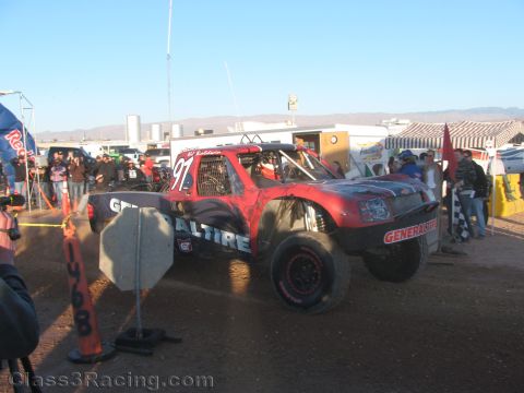 1990 Ford Bronco - red off-road race truck numbered 97 with General Tire sponsorship sits in a dusty desert staging area with spectators.