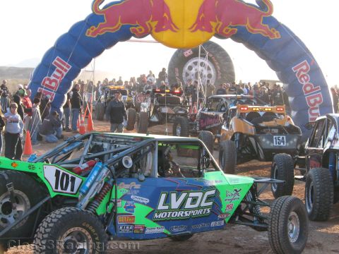1990 Ford Bronco - Green LVDC Motorsports buggy number 101 and other off-road cars including 154 stage under a Red Bull arch in warm low sun.