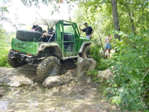 1992 Ford Bronco - Off-road vehicle tackling a challenging muddy and rocky course in a wooded area.