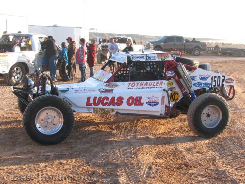 1990 Ford Bronco - white off-road race buggy numbered 1502 with Lucas Oil and Toyhauler graphics sits on dirt as crowds gather behind it.