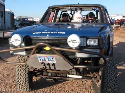 1990 Ford Bronco - Front view of a blue desertrat.com off-road race truck numbered 311 with a roof light bar, tube bumper and two crew aboard.