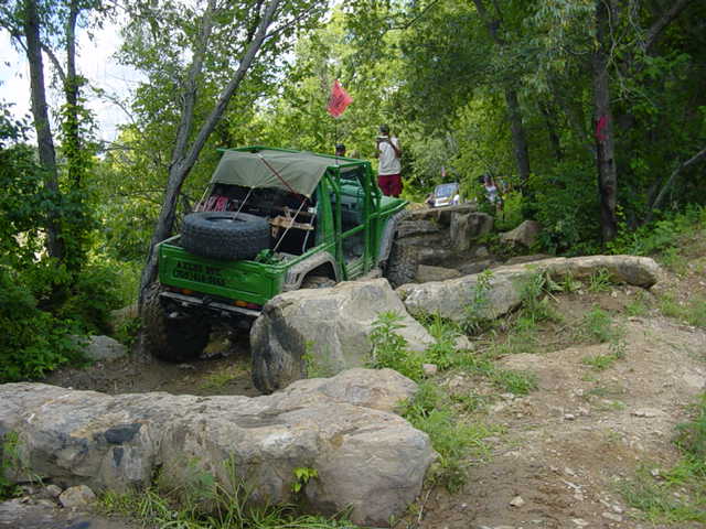 Green off-road vehicle with a spare tire on the back, navigating a rocky trail