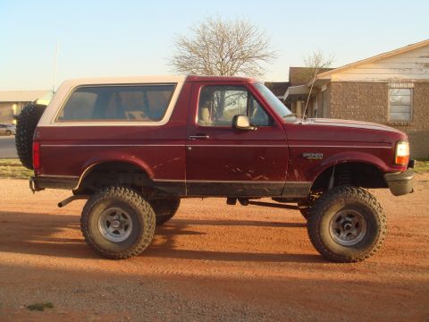 1992 Ford Bronco - This lifted 1992 Ford Bronco is parked on a dirt lot with a house in the background.