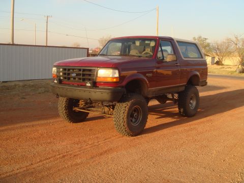 1992 Ford Bronco - A lifted red 1992 Ford Bronco is parked on a dirt road under a clear sky.