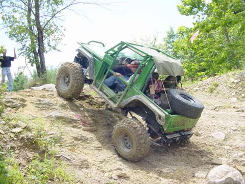 1992 Ford Bronco - A modified off-road vehicle navigates a steep, rocky incline with a driver and passenger inside.