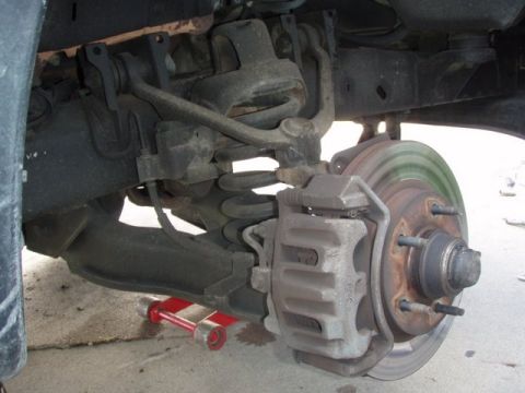 2007 Ford Mustang - Close-up view of a vehicle's front suspension and brake components, with a red jack visible below.