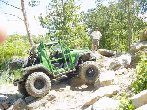 1992 Ford Bronco - An off-road vehicle navigates a rocky trail with a person observing from the side.