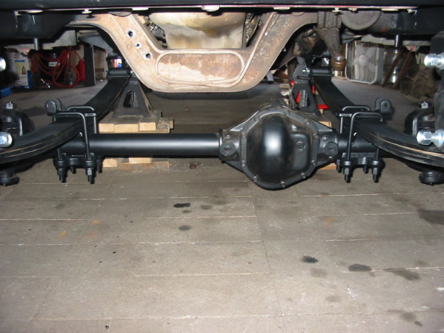 Black rear axle and differential with leaf springs under a truck in a garage