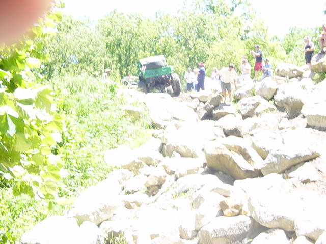 Green off-road vehicle on rocky terrain with spectators