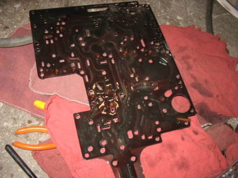 1995 Ford C-350 (Centurion Conversions) - A transmission valve body, covered in fluid, rests on red shop rags with tools nearby.