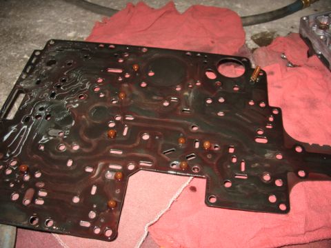 1995 Ford C-350 (Centurion Conversions) - Close-up of a transmission valve body plate with fluid residue and small spherical components.