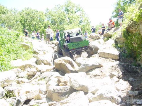 1992 Ford Bronco - An off-road vehicle navigates a challenging rocky path with spectators watching from the side.