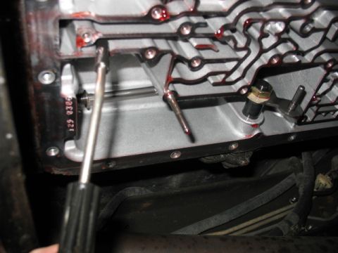 1995 Ford C-350 (Centurion Conversions) - Close-up view of a transmission pan interior, showing internal components and a screwdriver. Part numbers are visible on the casing.