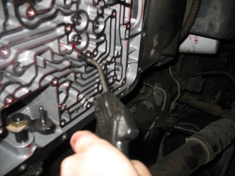 1995 Ford C-350 (Centurion Conversions) - Close-up of a transmission valve body with red fluid visible, and a tool being used.