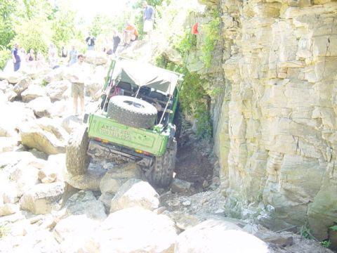 1992 Ford Bronco - A green off-road vehicle navigates a challenging rocky terrain next to a sheer cliff face.