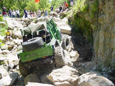 1992 Ford Bronco - A green off-road vehicle attempts to climb a steep, rocky terrain with spectators watching.