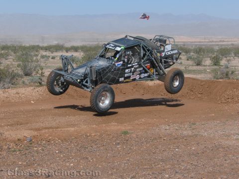 1990 Ford Bronco - black exposed tube-frame off-road race buggy, numbered 1206 with Yokohama livery, jumps a desert dirt course.