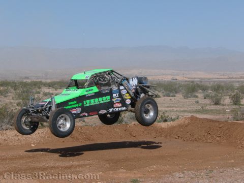 1990 Ford Bronco - green-and-black off-road race buggy numbered 1400 leaps off a dirt berm in a desert race setting.