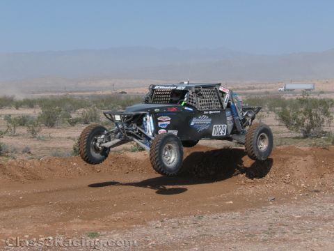1990 Ford Bronco - black off-road race buggy numbered 1029 leaps over a dirt berm on an open desert race course.