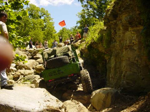 1992 Ford Bronco - A green off-road vehicle tackles a challenging rocky trail with spectators watching from the side.