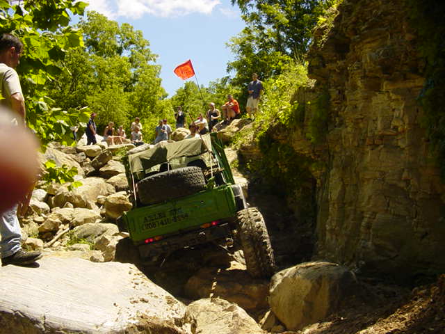 Green off-road vehicle with spare tires on back, climbing rocks