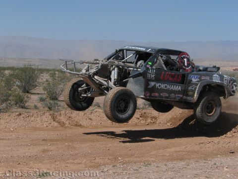 1990 Ford Bronco - dark Lucas/Yokohama-sponsored No. 1 tube-chassis race truck leaps a dirt jump, exposed long-travel suspension visible.
