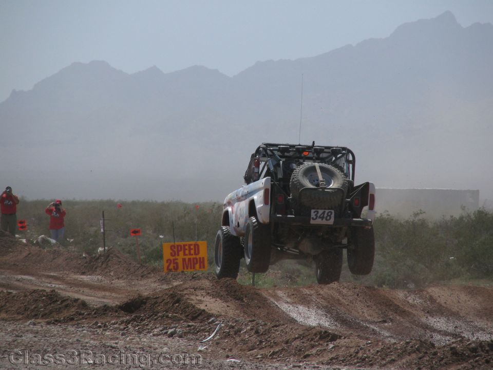 Rear view of off-road race truck No. 348 airborne in hazy desert dust