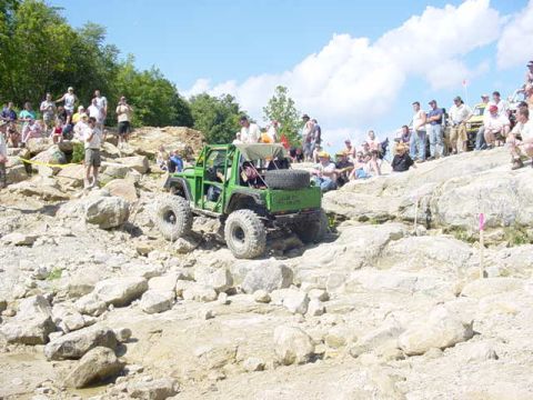 1992 Ford Bronco - A crowd watches a modified green off-road vehicle navigate a challenging rocky terrain.